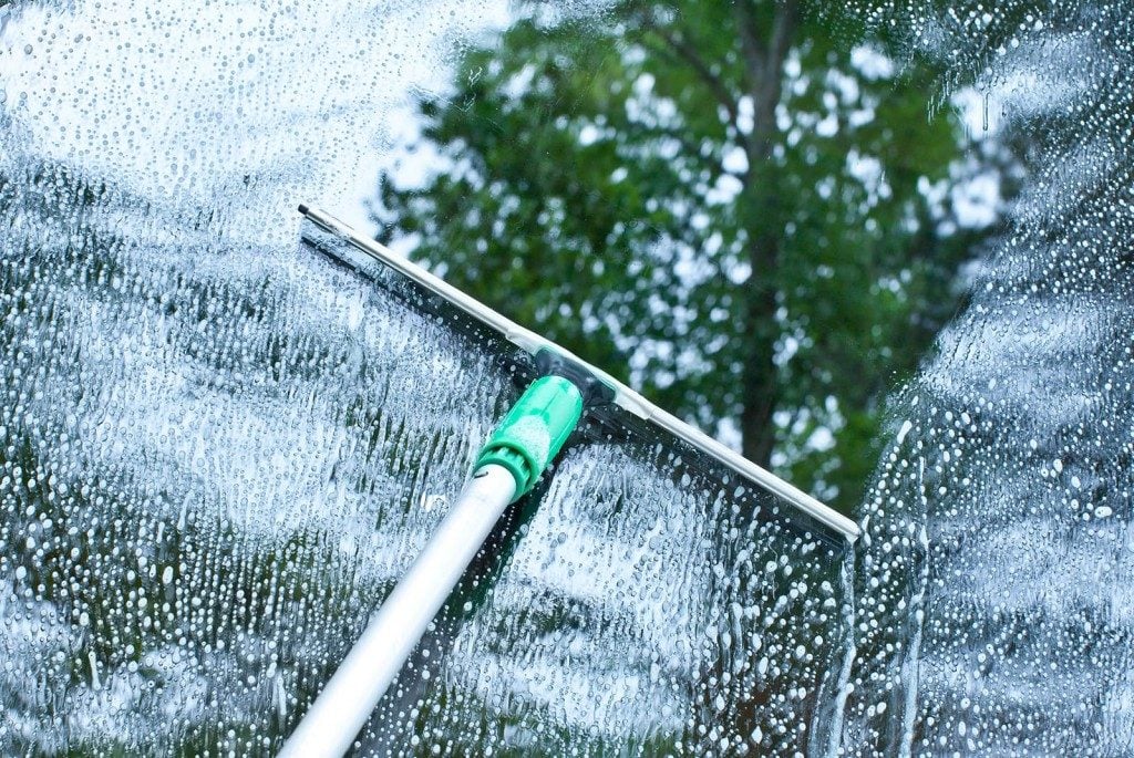 Close-up of a squeegee cleaning soapy residential glass