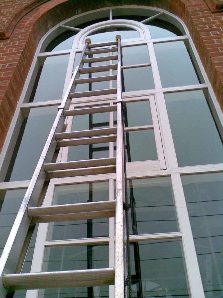 Ladder set against a tall glass facade for high-access cleaning